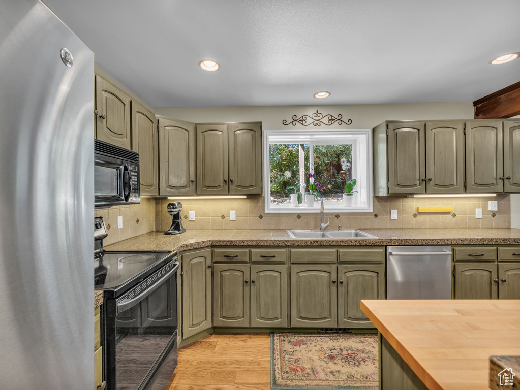 Kitchen with black appliances, light wood-style floors, decorative backsplash, recessed lighting, and wood counters