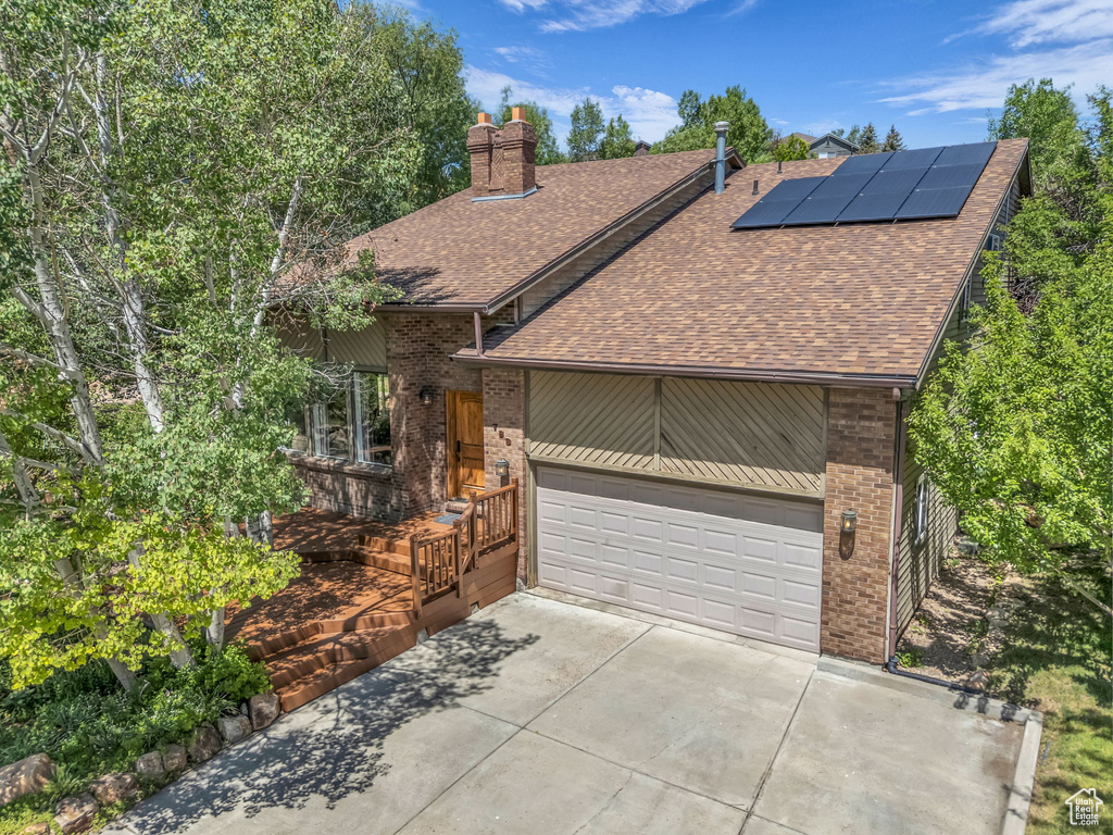 View of front of house with a shingled roof, brick siding, roof mounted solar panels, driveway, and a chimney