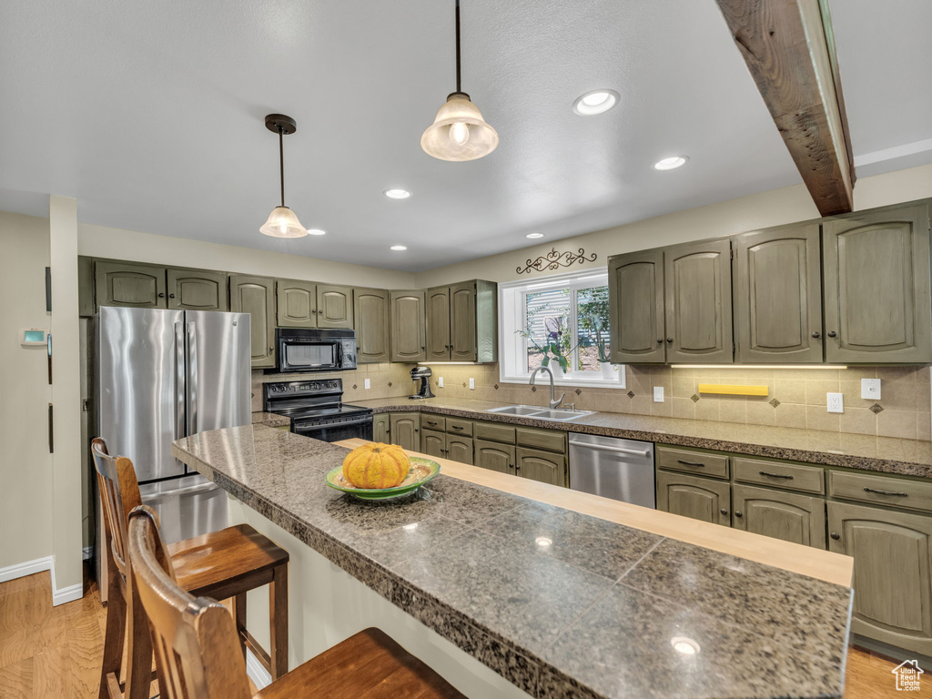 Kitchen with black appliances, a breakfast bar area, light wood-type flooring, backsplash, and recessed lighting