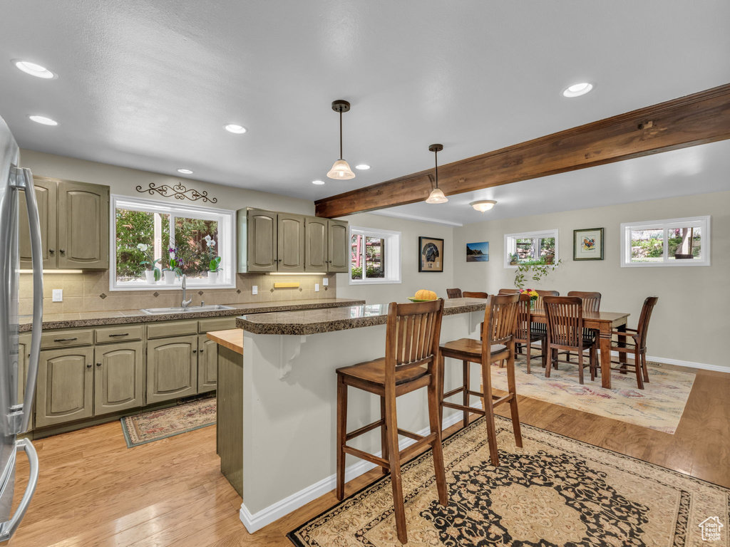 Kitchen with a kitchen bar, light wood-type flooring, recessed lighting, freestanding refrigerator, and beam ceiling