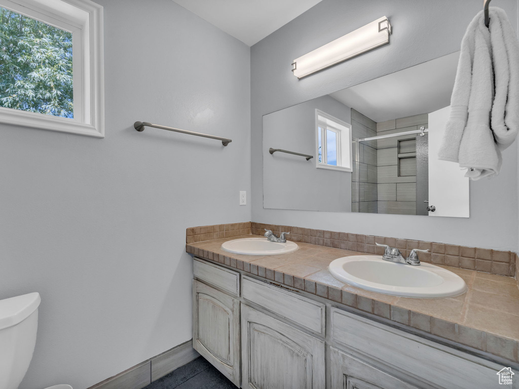 Full bath with tiled shower, double vanity, and tile patterned flooring