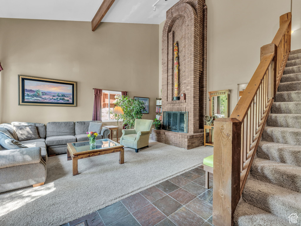 Living room with a towering ceiling, stone tile flooring, a fireplace, beam ceiling, and stairs