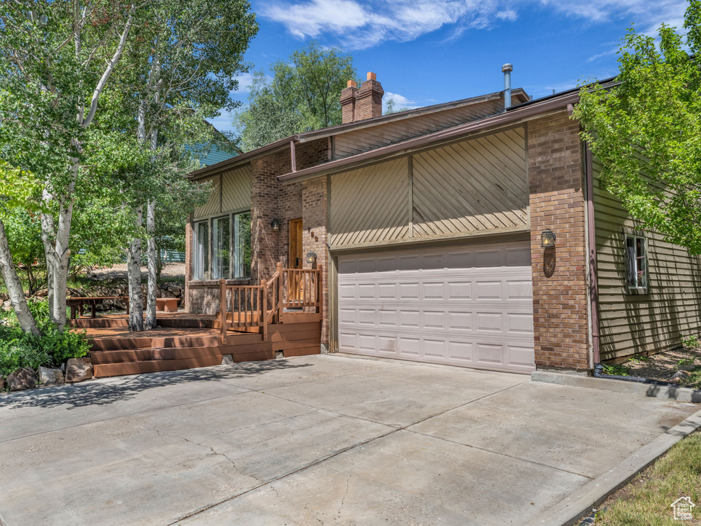 View of front facade featuring brick siding, a chimney, concrete driveway, and an attached garage