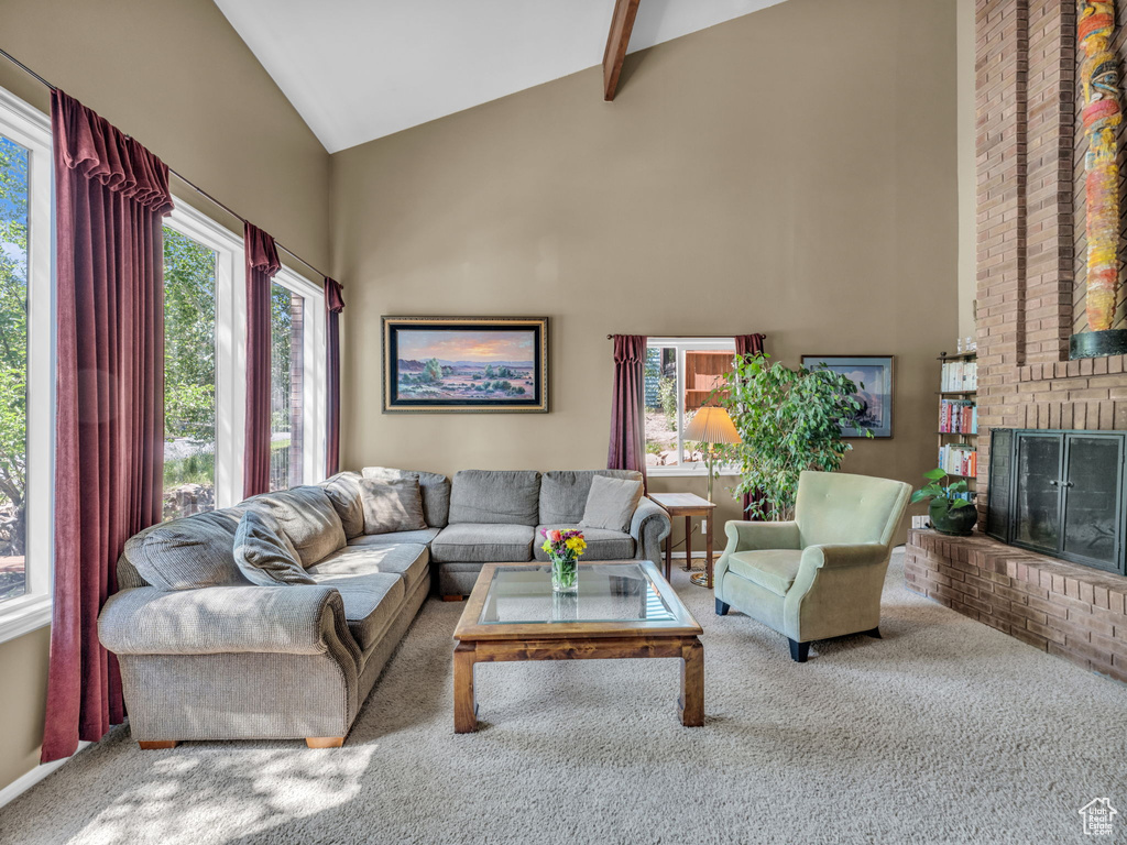 Living area with high vaulted ceiling, carpet flooring, plenty of natural light, a fireplace, and beamed ceiling