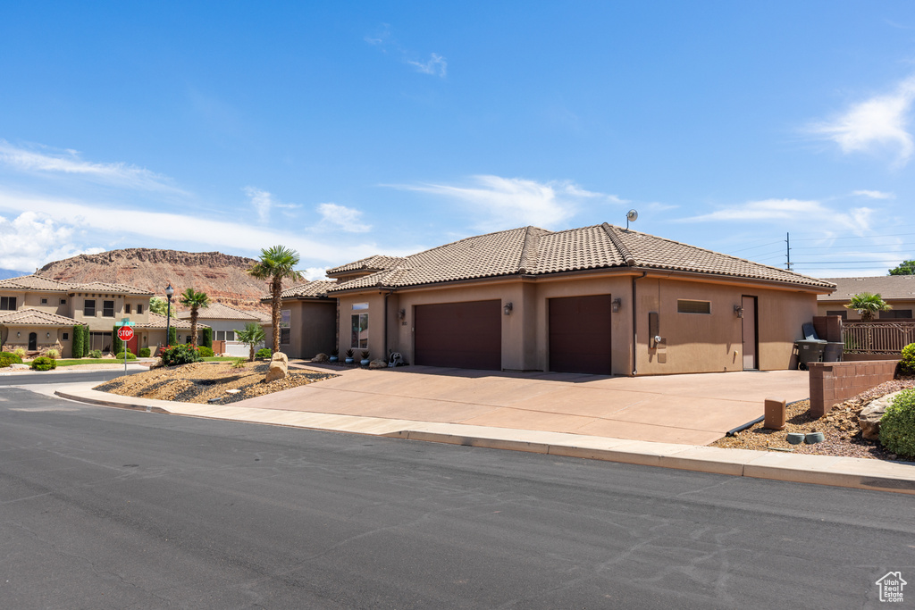 View of front facade featuring stucco siding, a tile roof, an attached garage, and driveway