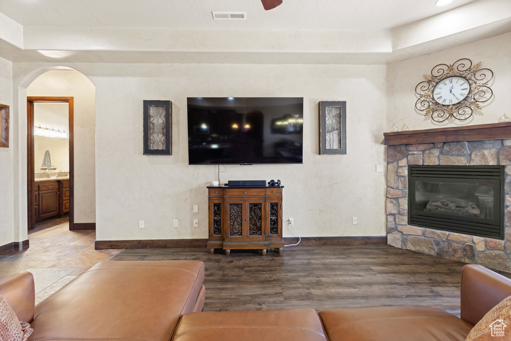 Living room with a fireplace, arched walkways, wood finished floors, and a raised ceiling
