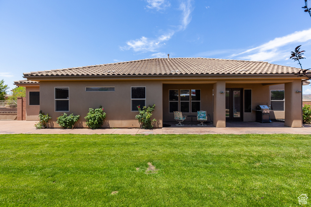 Rear view of property with a tiled roof, stucco siding, a yard, and a patio area