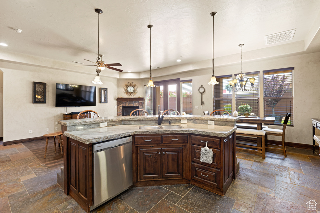 Kitchen featuring stainless steel dishwasher, stone tile flooring, a tray ceiling, a fireplace, and a ceiling fan