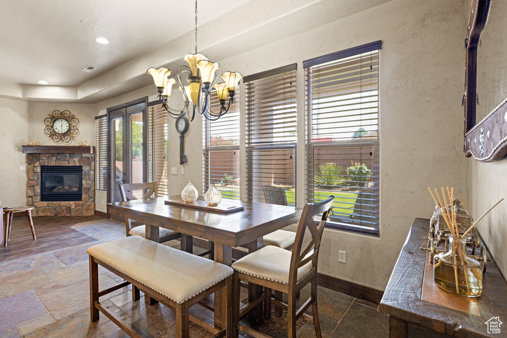 Dining area with stone tile floors, a stone fireplace, a chandelier, a textured wall, and recessed lighting