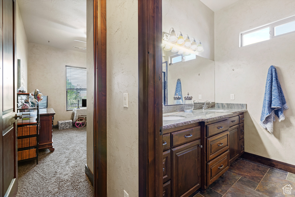 Full bath with double vanity, plenty of natural light, and stone finish floors