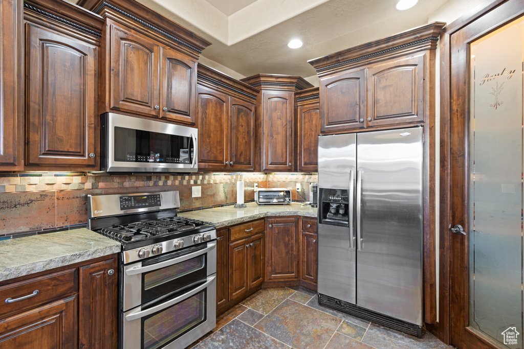 Kitchen featuring appliances with stainless steel finishes, stone tile flooring, tasteful backsplash, recessed lighting, and light stone countertops