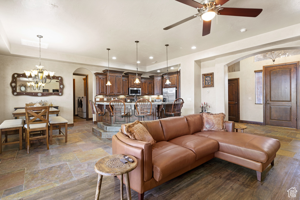 Living room featuring arched walkways, stone tile flooring, a chandelier, washer / dryer, and a ceiling fan