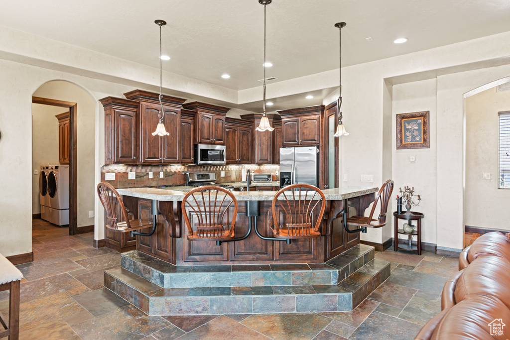 Kitchen featuring appliances with stainless steel finishes, arched walkways, stone tile floors, washing machine and clothes dryer, and recessed lighting