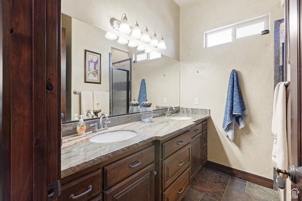 Bathroom featuring double vanity, a shower with shower door, and stone finish flooring