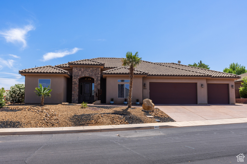 Mediterranean / spanish-style house with stucco siding, a garage, concrete driveway, stone siding, and a tile roof