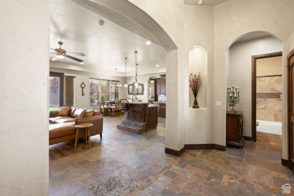 Living room featuring arched walkways, stone tile floors, ceiling fan, and a textured wall