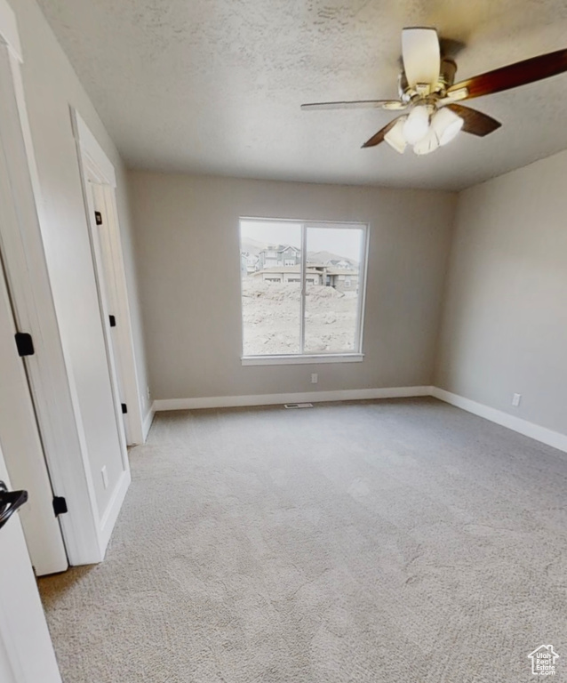 Carpeted empty room with a ceiling fan and a textured ceiling