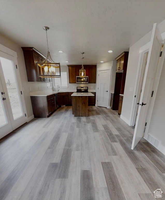 Kitchen with stainless steel microwave, range, a center island, recessed lighting, and light wood-style floors