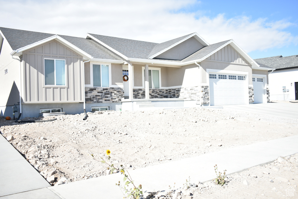 View of front of home featuring board and batten siding, an attached garage, covered porch, and a shingled roof