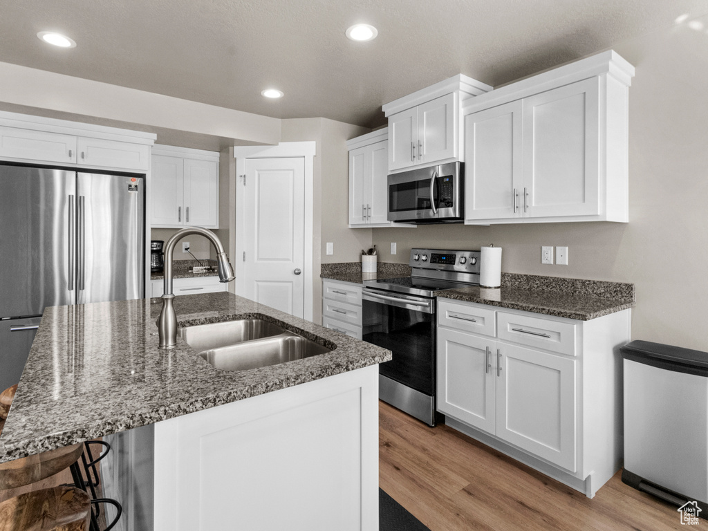 Kitchen with appliances with stainless steel finishes, light wood-style floors, white cabinetry, recessed lighting, and dark stone countertops