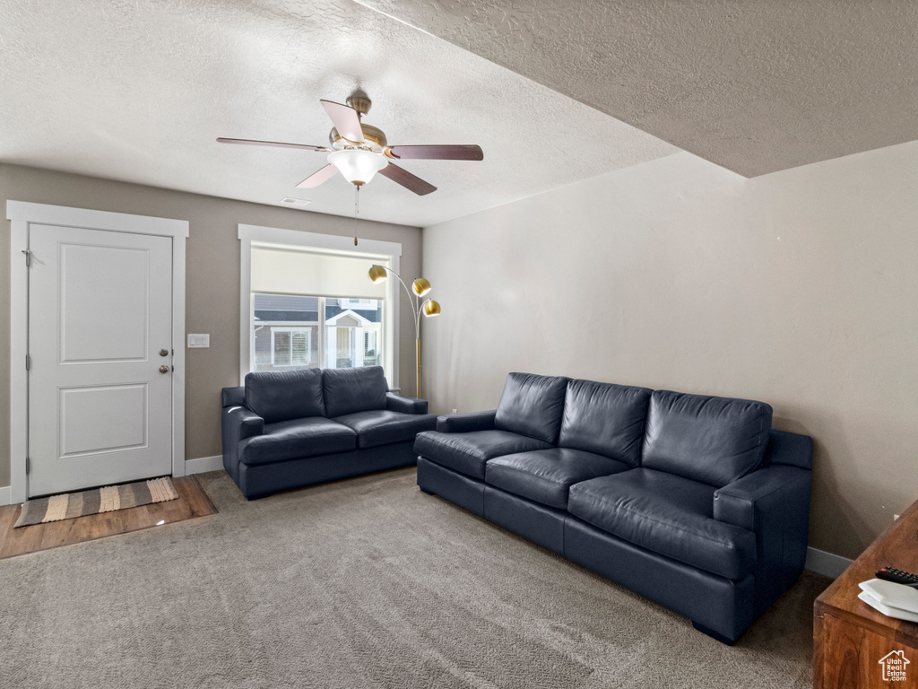 Living area featuring carpet flooring, ceiling fan, and a textured ceiling