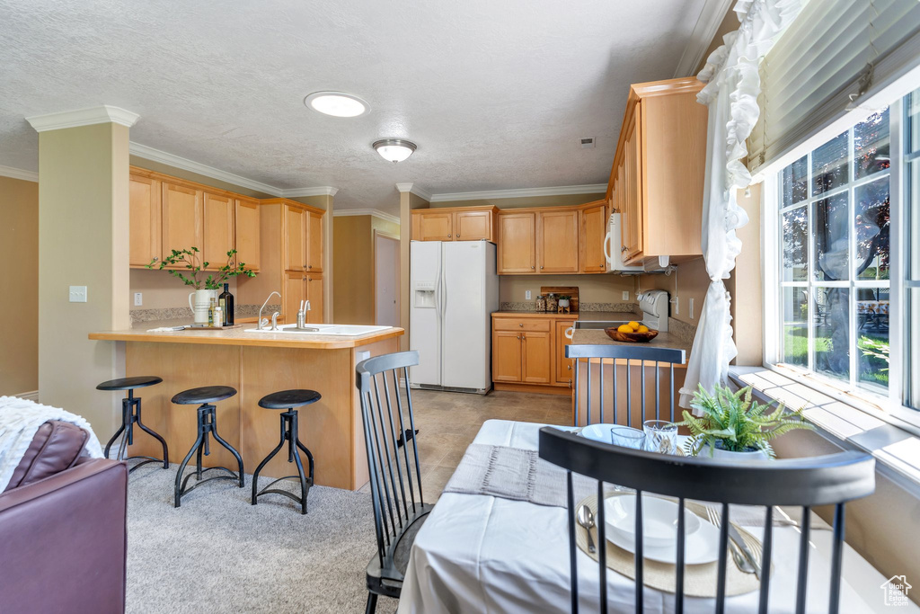Kitchen featuring white refrigerator with ice dispenser, a peninsula, crown molding, a kitchen bar, and a textured ceiling