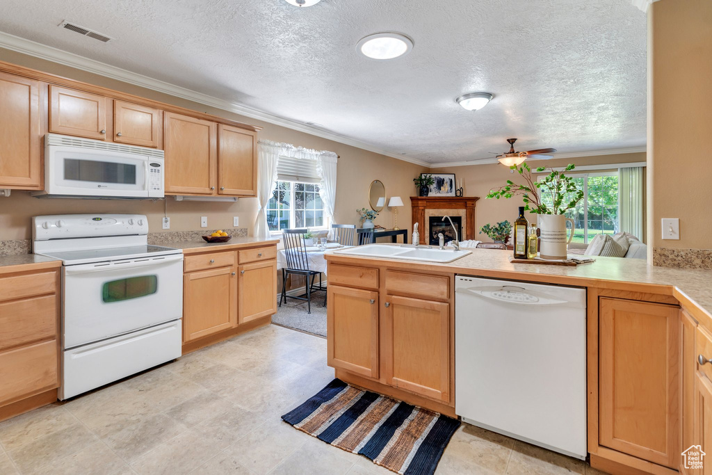 Kitchen featuring white appliances, a textured ceiling, healthy amount of natural light, a peninsula, and ornamental molding