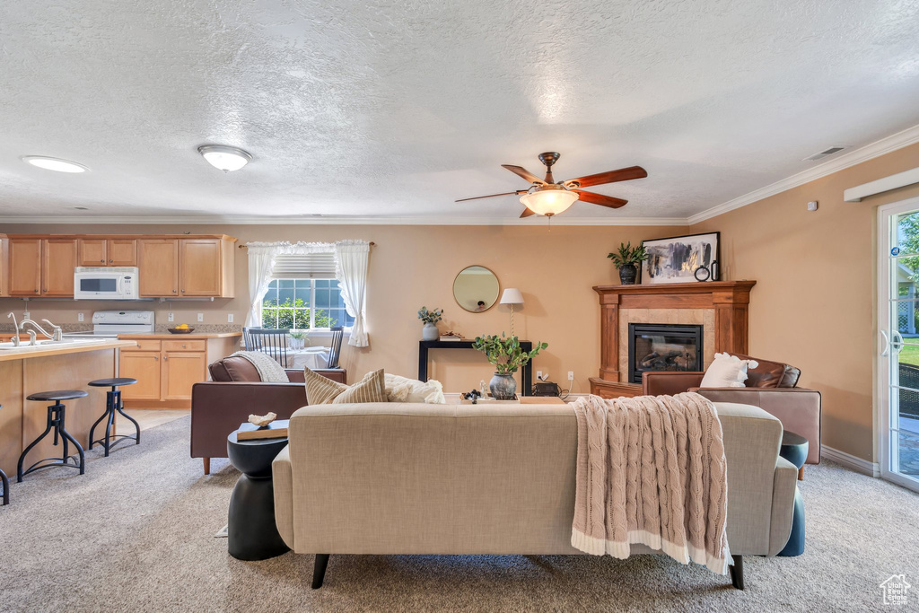 Living area featuring plenty of natural light, a tile fireplace, light carpet, crown molding, and a ceiling fan