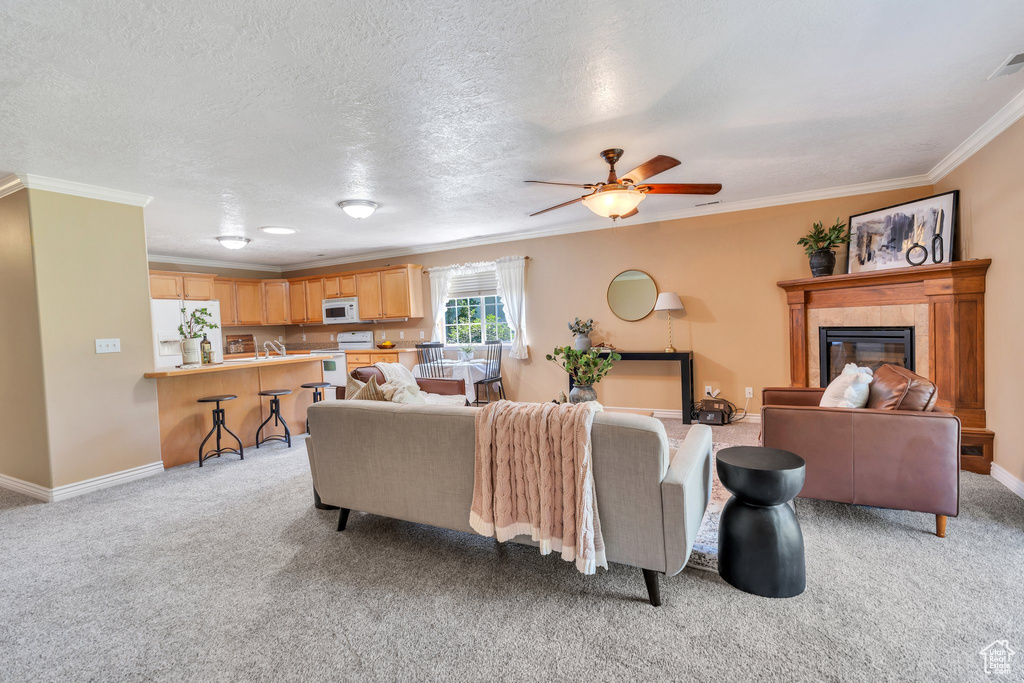 Living room featuring crown molding, light colored carpet, a tiled fireplace, a ceiling fan, and a textured ceiling
