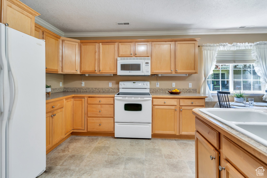 Kitchen with white appliances, crown molding, light countertops, a textured ceiling, and light brown cabinets