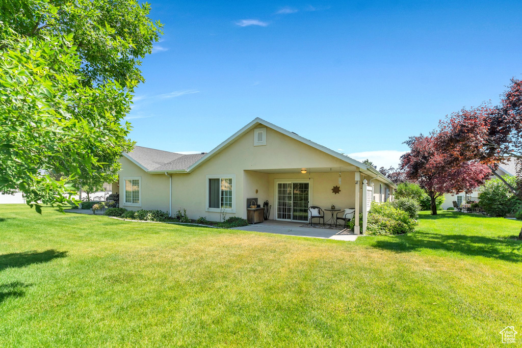 Back of property with stucco siding, a patio area, and a lawn