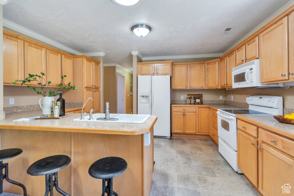 Kitchen with white appliances, a peninsula, a kitchen breakfast bar, crown molding, and light countertops