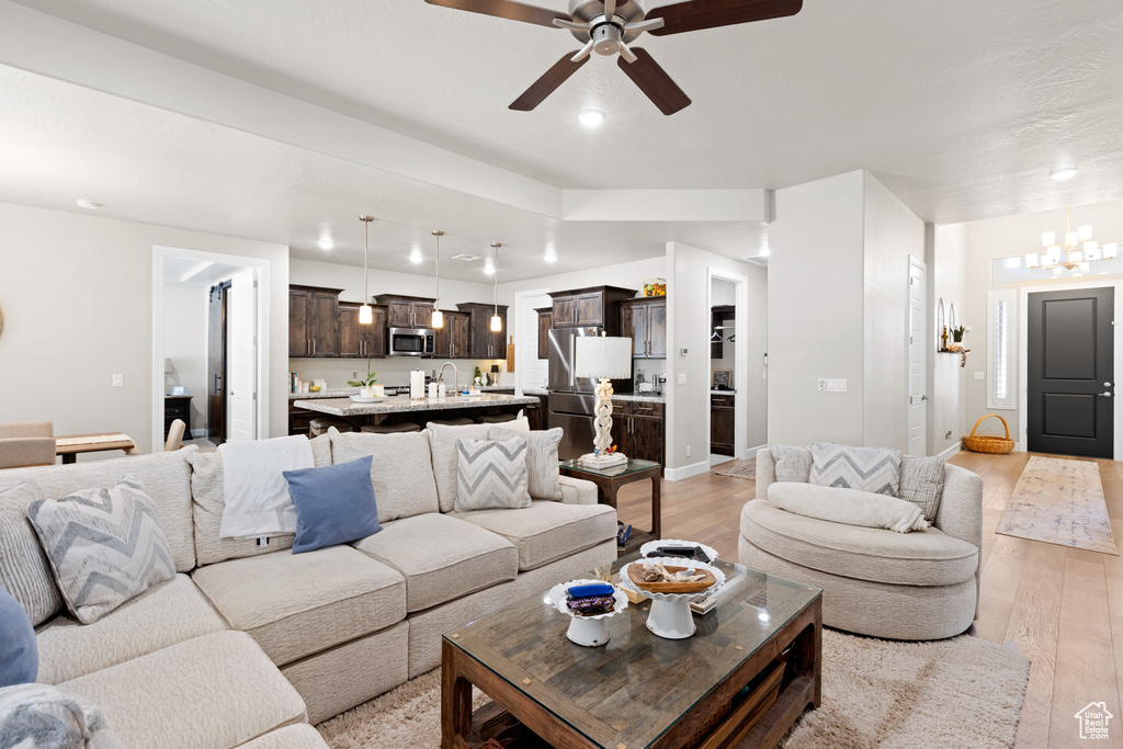 Living room with light wood-style floors, a ceiling fan, recessed lighting, and a chandelier