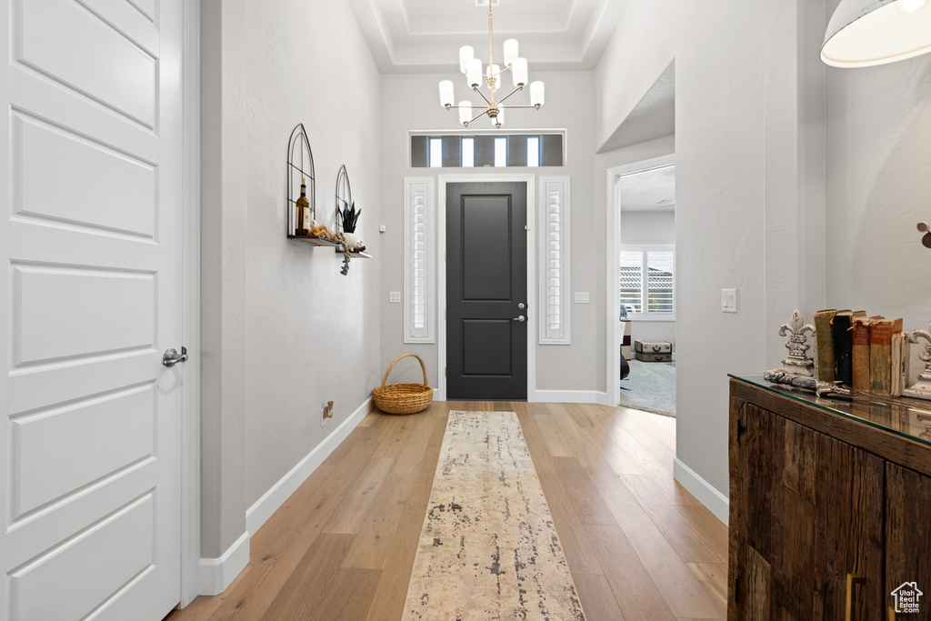 Foyer entrance featuring light wood-type flooring, a chandelier, a raised ceiling, and crown molding