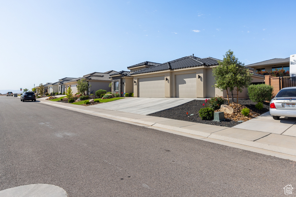 View of front facade with an attached garage, stucco siding, driveway, a residential view, and a tile roof