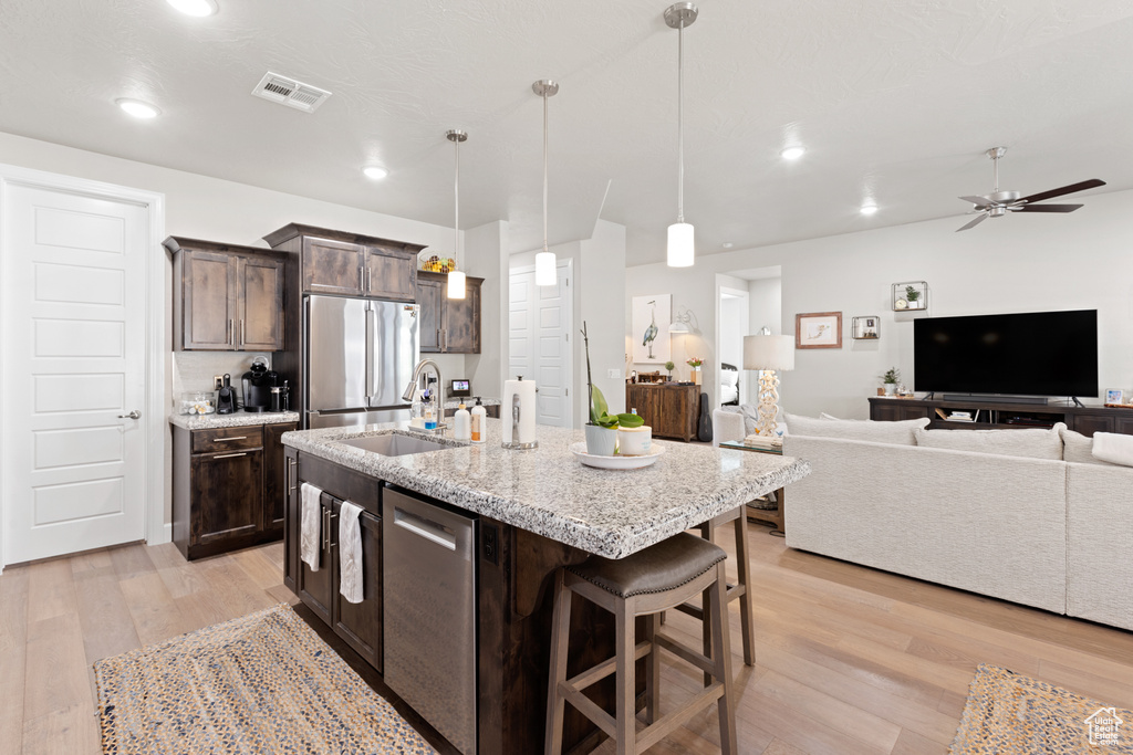 Kitchen with stainless steel appliances, light wood-style floors, dark brown cabinetry, open floor plan, and ceiling fan