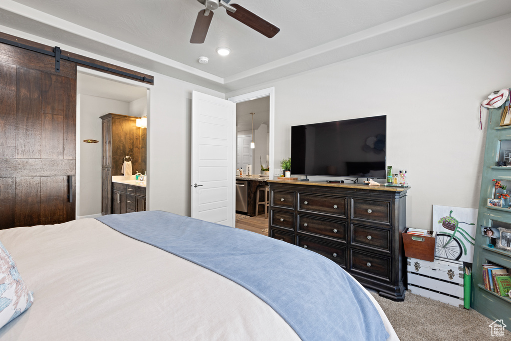 Bedroom with ensuite bathroom, a barn door, carpet floors, and a ceiling fan