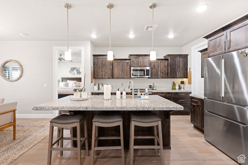 Kitchen with appliances with stainless steel finishes, dark brown cabinets, a kitchen bar, light wood-style floors, and recessed lighting