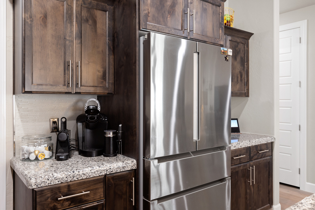 Kitchen featuring freestanding refrigerator, dark brown cabinetry, backsplash, light stone counters, and light wood-style floors