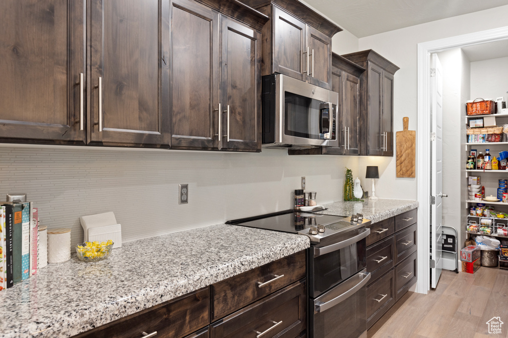 Kitchen featuring stainless steel appliances, dark brown cabinets, light stone counters, and light wood finished floors