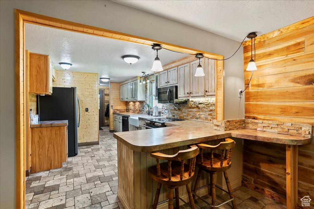 Kitchen featuring black appliances, a peninsula, a textured ceiling, a kitchen bar, and pendant lighting