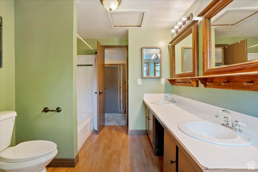 Full bathroom featuring wood finished floors, double vanity, a textured ceiling, and shower / washtub combination