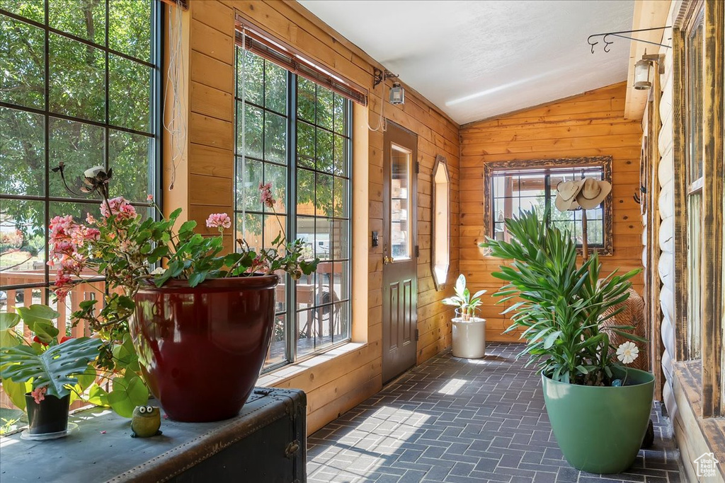 Doorway featuring wooden walls, lofted ceiling, and brick patterned floors