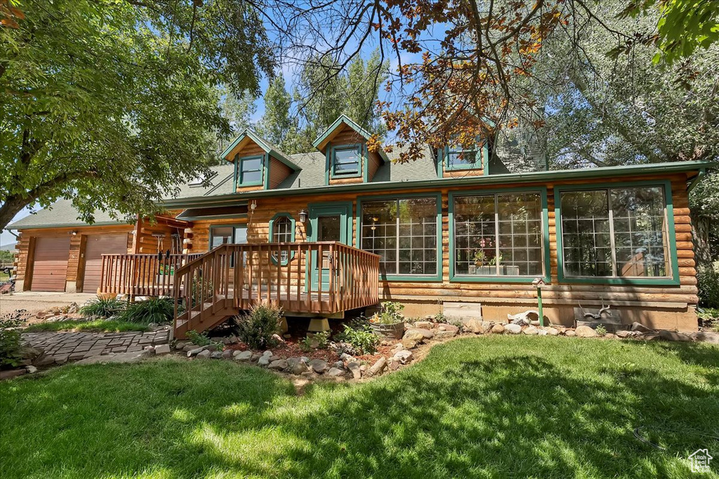 Back of house with a lawn, a wooden deck, driveway, and a garage