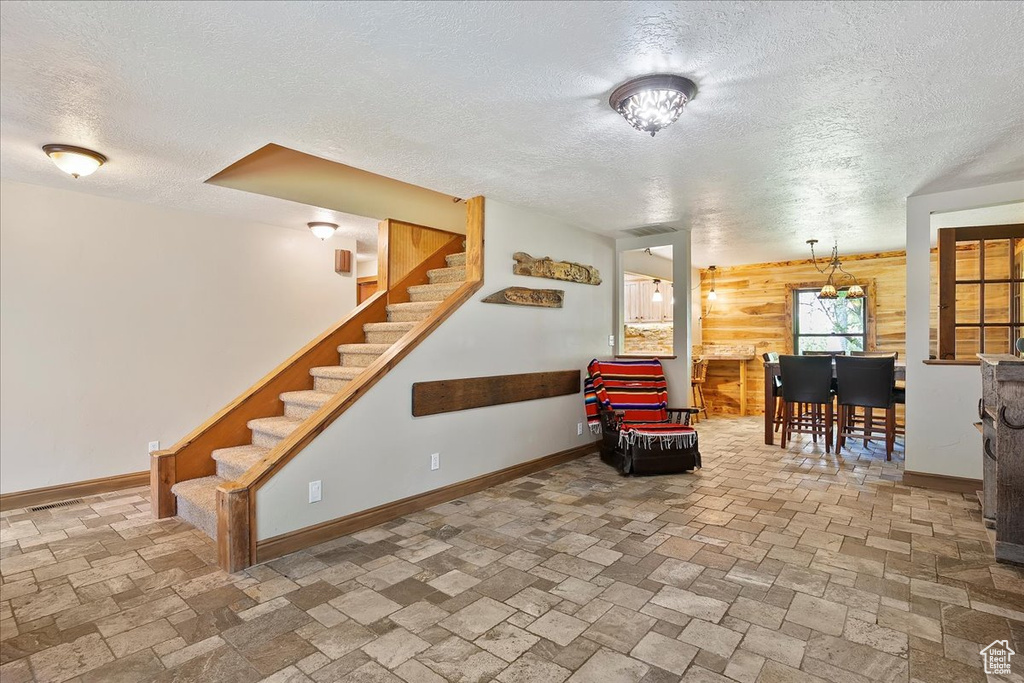 Living area featuring a textured ceiling, wooden walls, stone tile flooring, and stairs