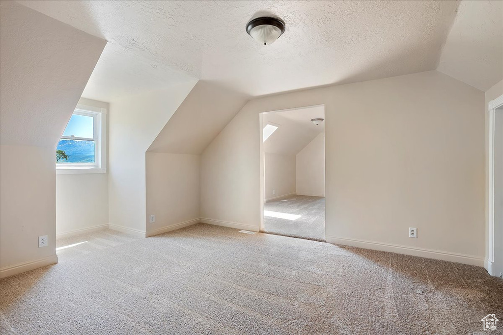 Additional living space featuring vaulted ceiling, light carpet, and a textured ceiling