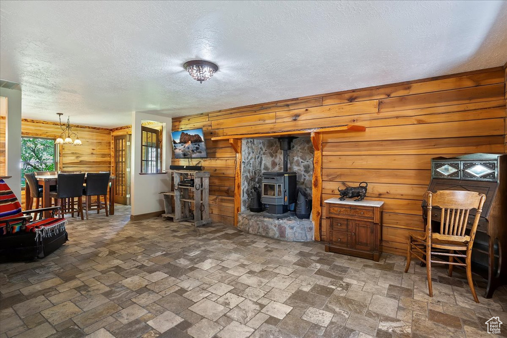 Living area featuring wood walls, a chandelier, a wood stove, a textured ceiling, and stone tile flooring
