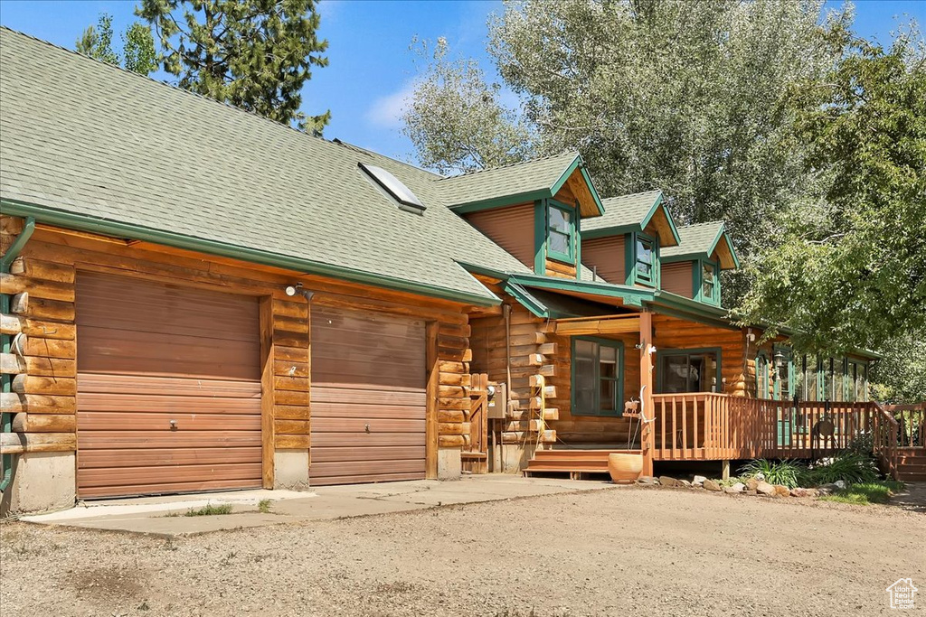 Log cabin with log exterior, a garage, a shingled roof, and driveway