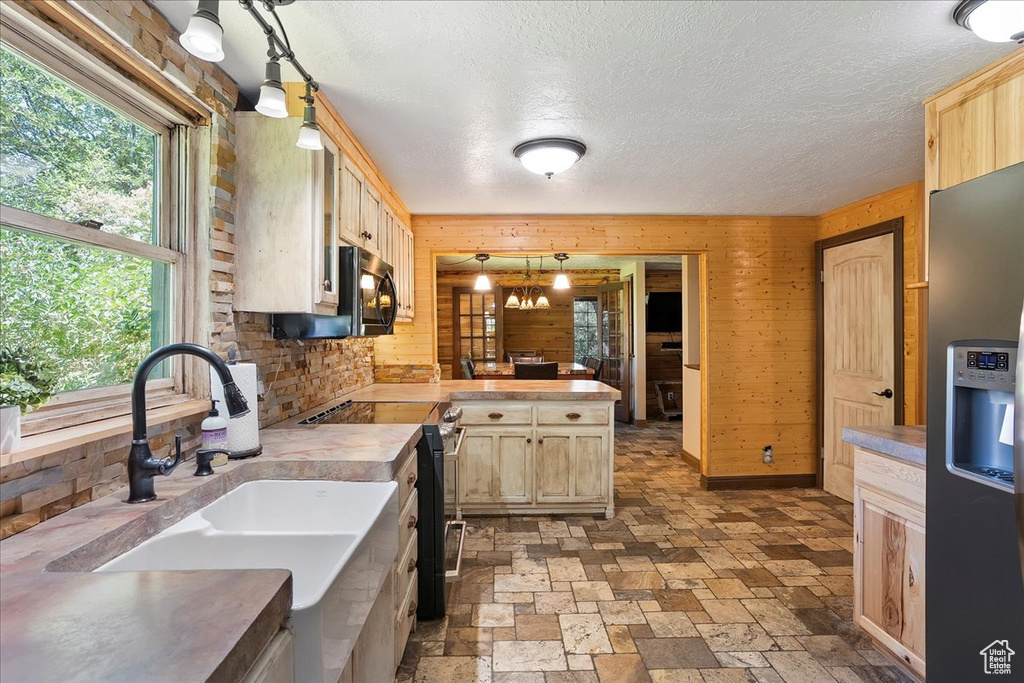 Kitchen featuring appliances with stainless steel finishes, wooden walls, a peninsula, light brown cabinetry, and light countertops