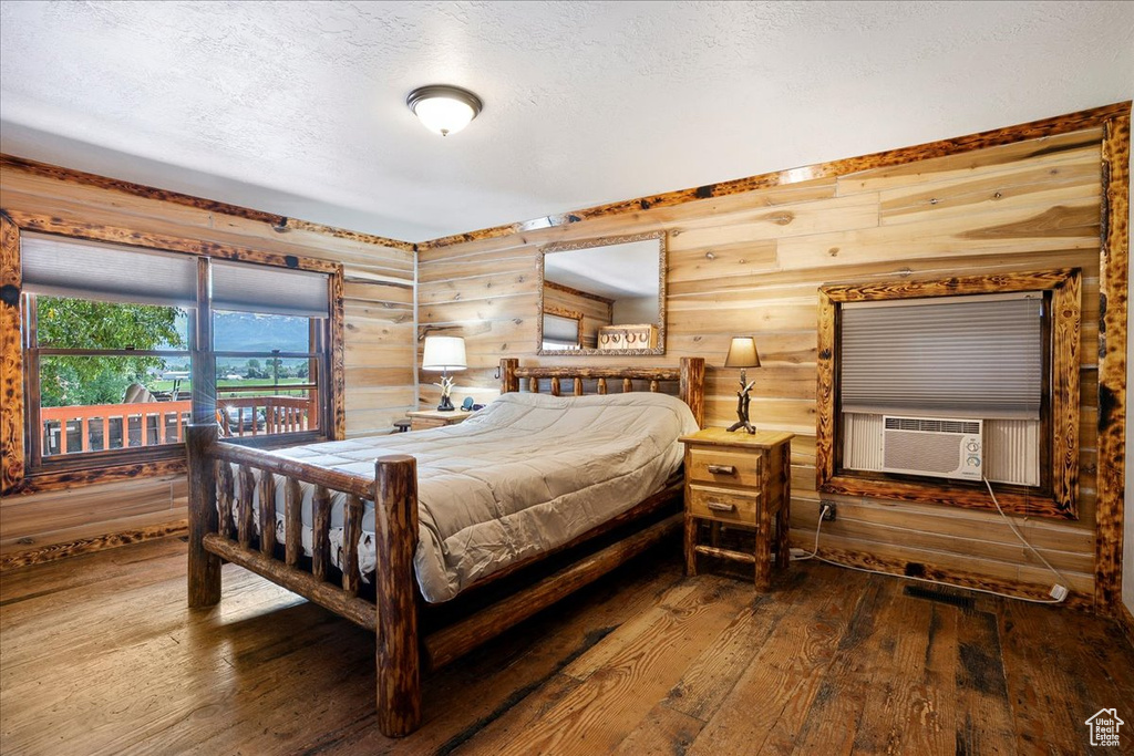 Bedroom with hardwood / wood-style floors, a textured ceiling, cooling unit, and wooden walls
